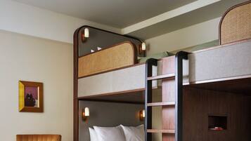A bunk bed room with a wooden ladder, a cushioned chair, a small table with books, and a framed picture on the wall.