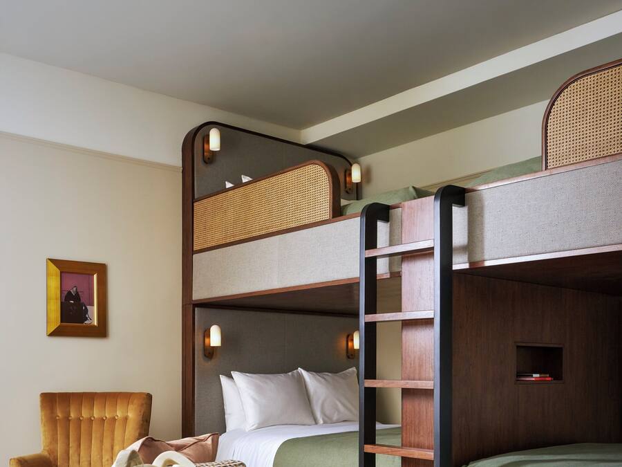 Habitación con literas, una escalera de madera, un sillón acolchado, una mesita con libros y un cuadro en la pared.