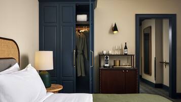 Een hotelkamer met een bed, nachtkastje, kledingkast, spiegel, een plank met toiletartikelen en een wandlamp.