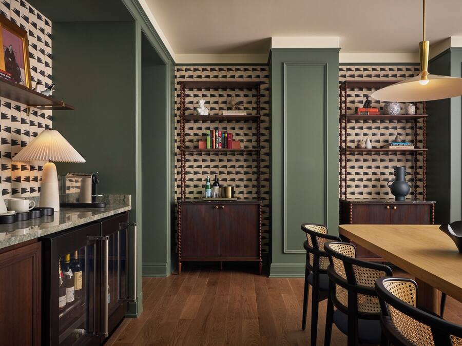 Un comedor con una mesa y sillas de madera, una lámpara colgante y un papel tapiz estampado.