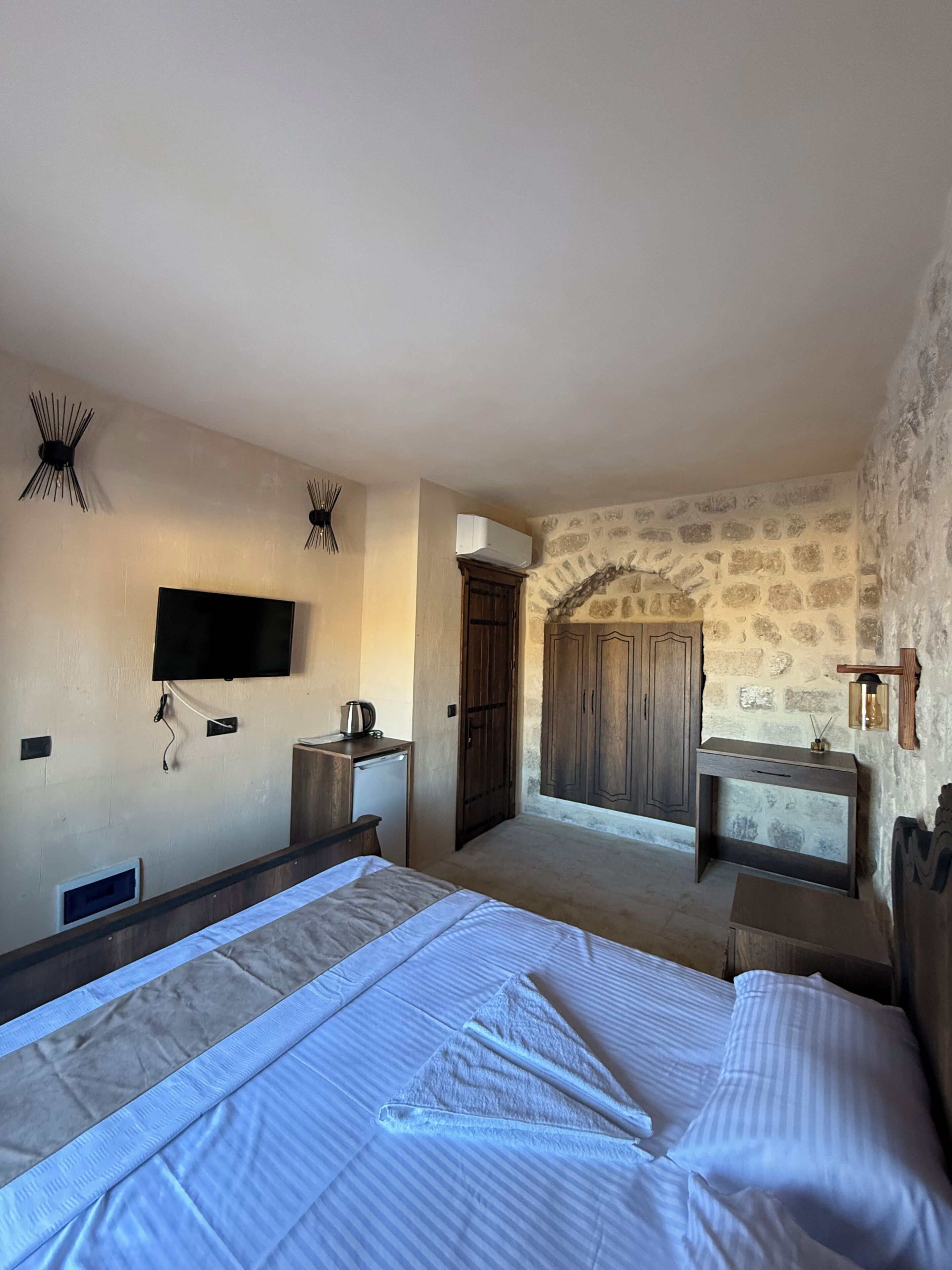 Een hotelkamer met een bed, een bureau, een televisie en een stenen muur.
