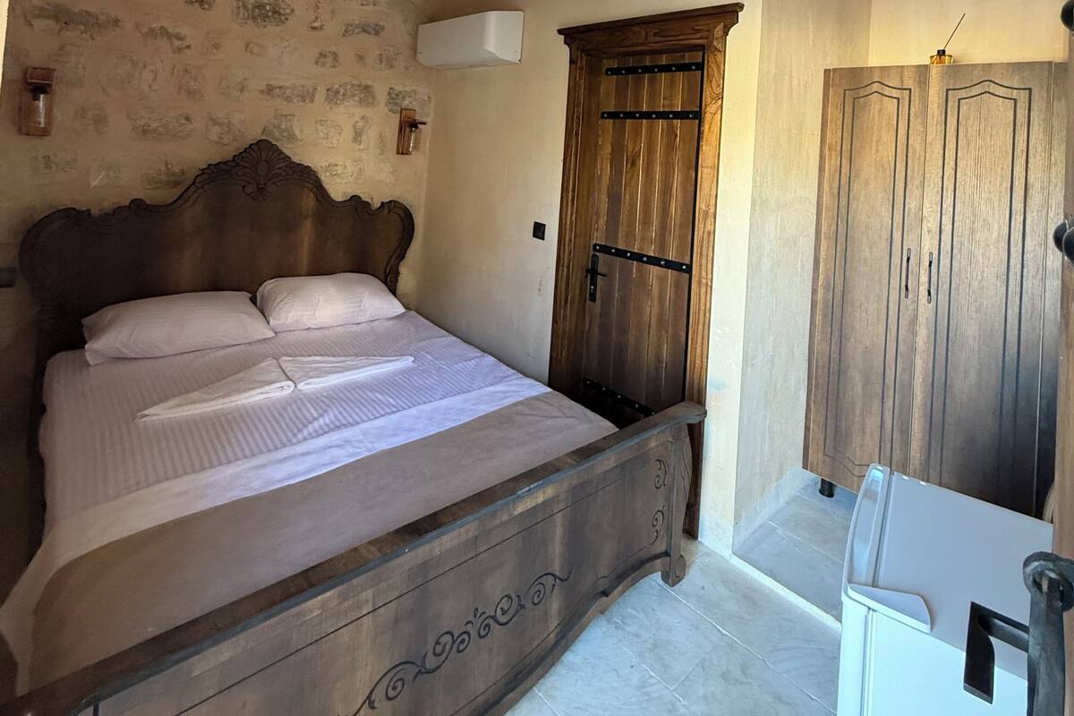 A bedroom with a wooden bed, a stone wall, a wardrobe, and a bathroom with a white sink.
