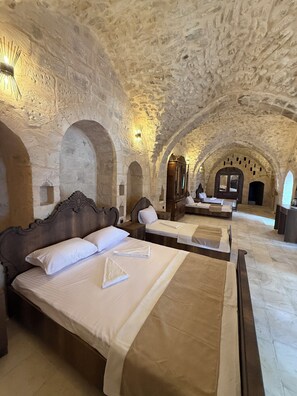 A hotel room with stone walls, arched ceilings, and a large bed with a wooden headboard.