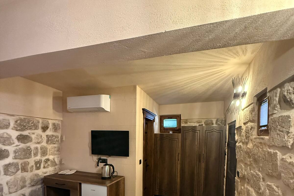 A bedroom with a bed, a small kitchenette, a TV, and a stone wall.