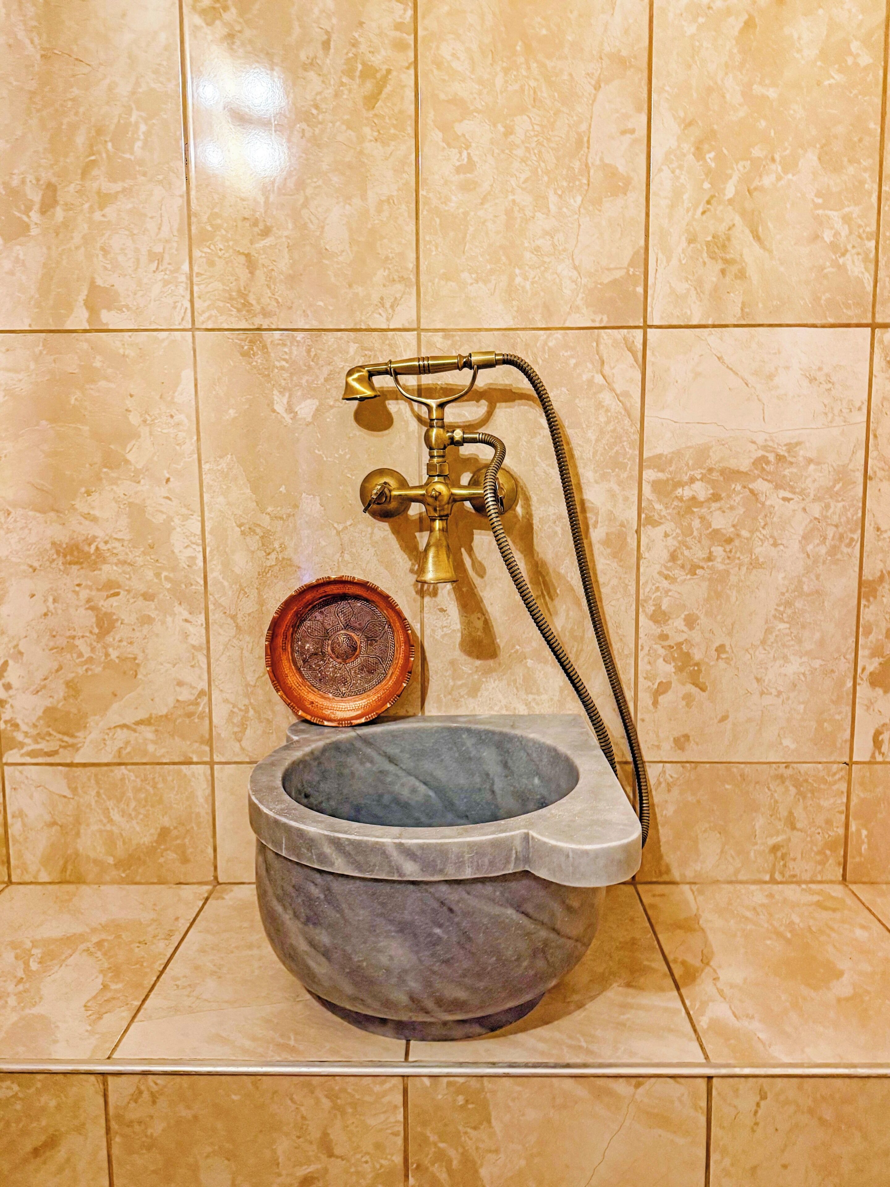 A bathroom with a marble sink, a brass faucet, and a decorative plate.