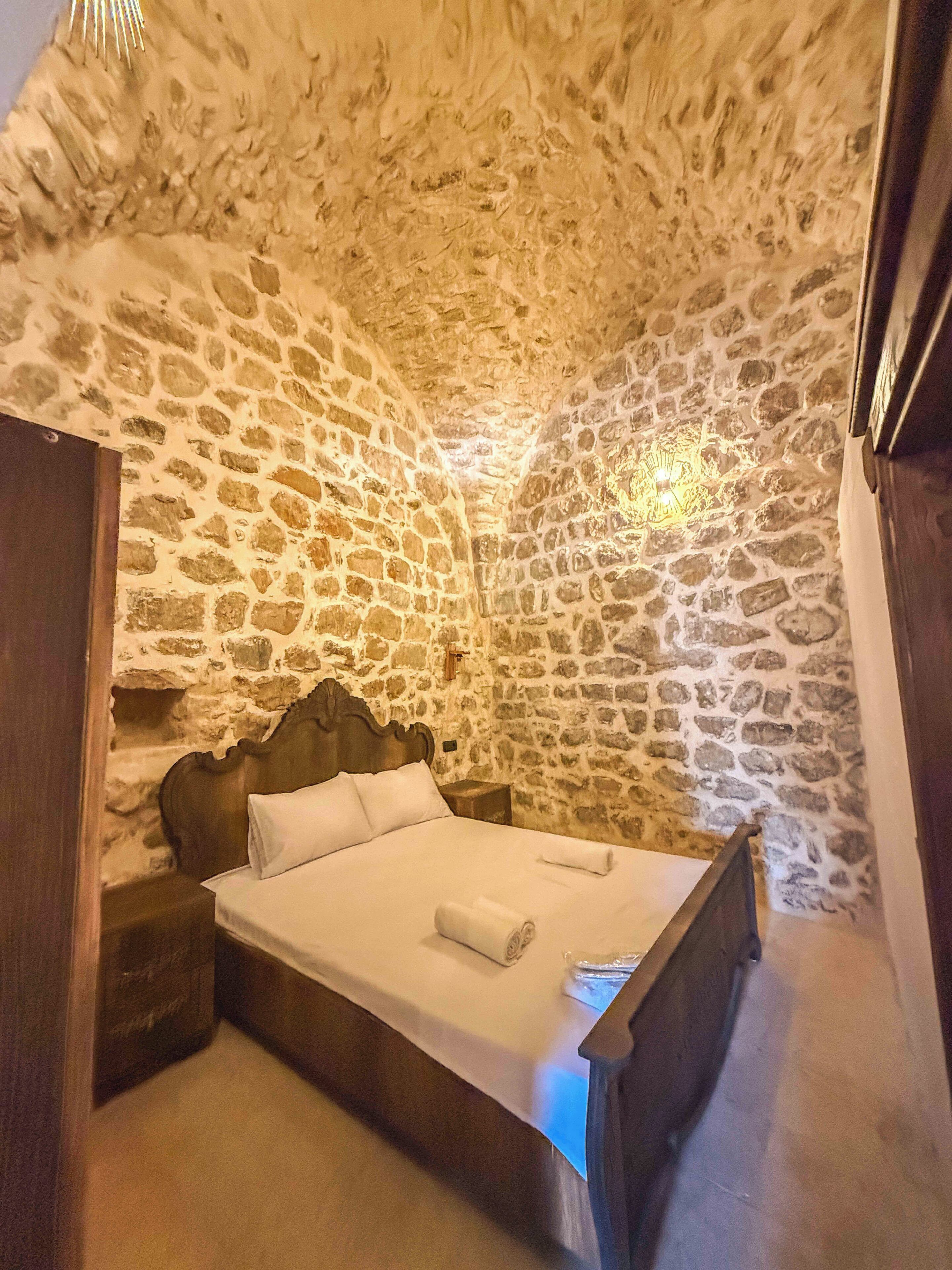 Un dormitorio con pared de piedra, estructura de cama de madera y una mesita de noche.