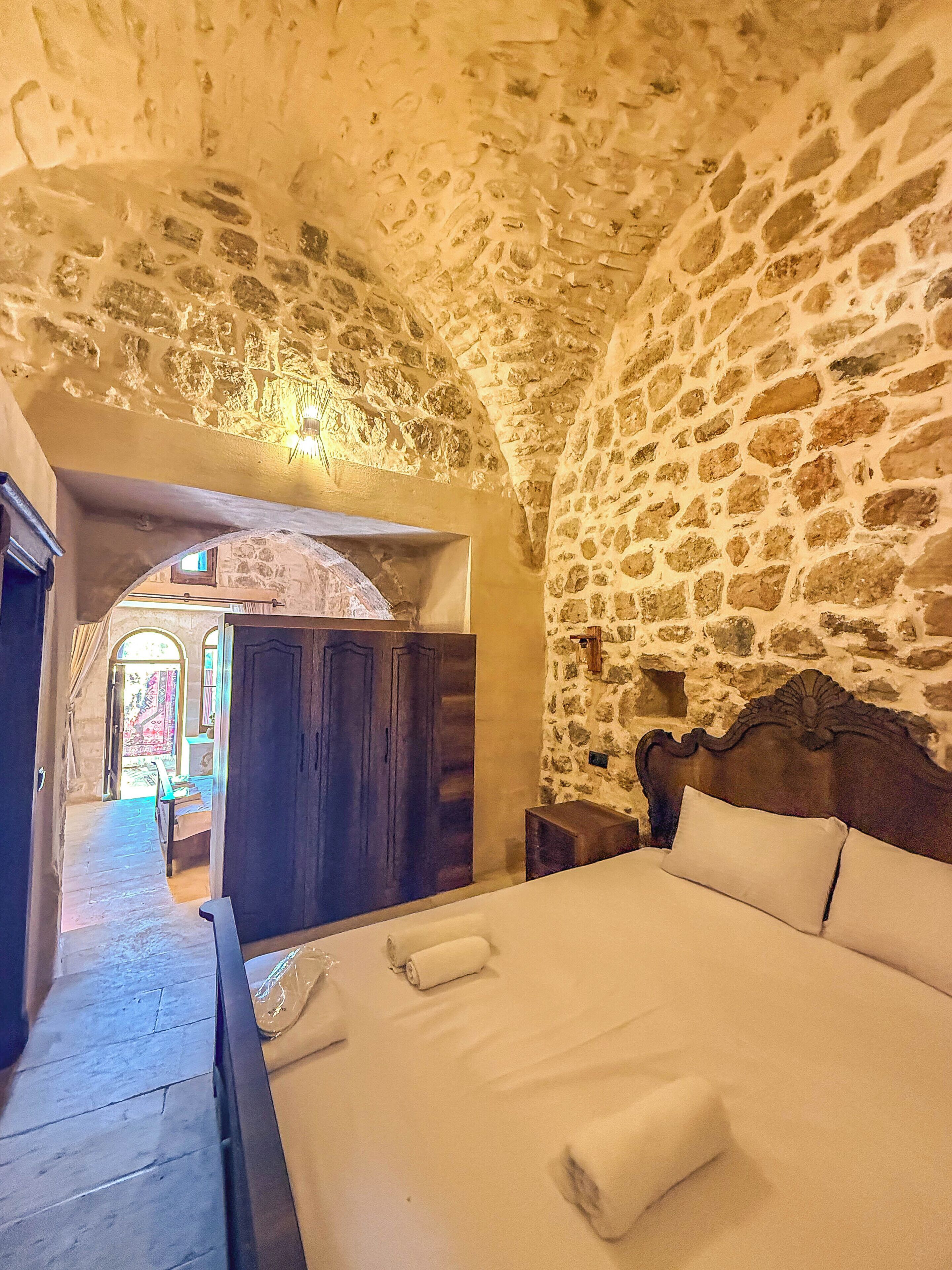 Habitació de parets de pedra amb un llit, un armari de fusta i una taula petita.