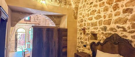 Habitació de parets de pedra amb un llit, un armari de fusta i una taula petita.