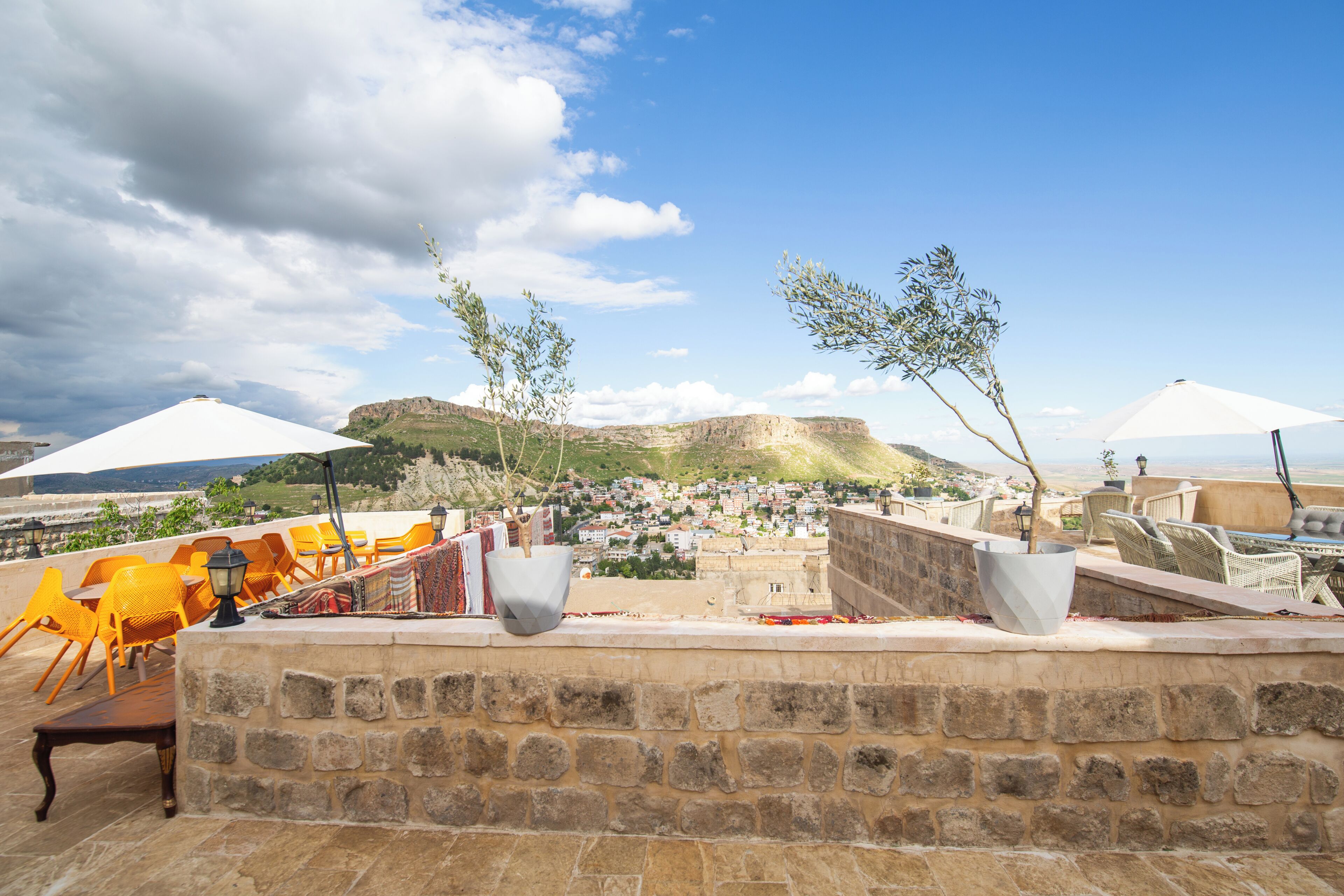 A terrace with stone walls, outdoor seating, and a view of a town and mountains.
