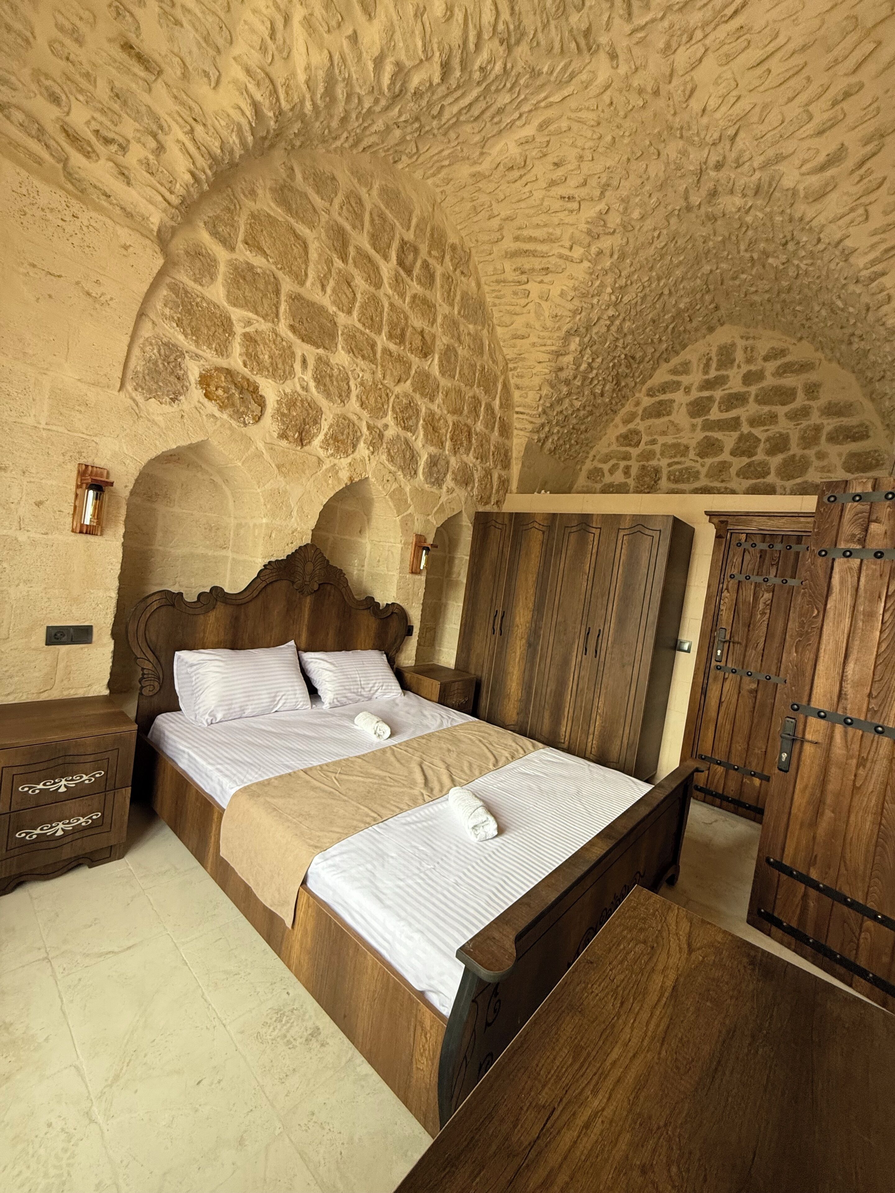 A stone-walled bedroom with a wooden bed, a wardrobe, and a chest of drawers.
