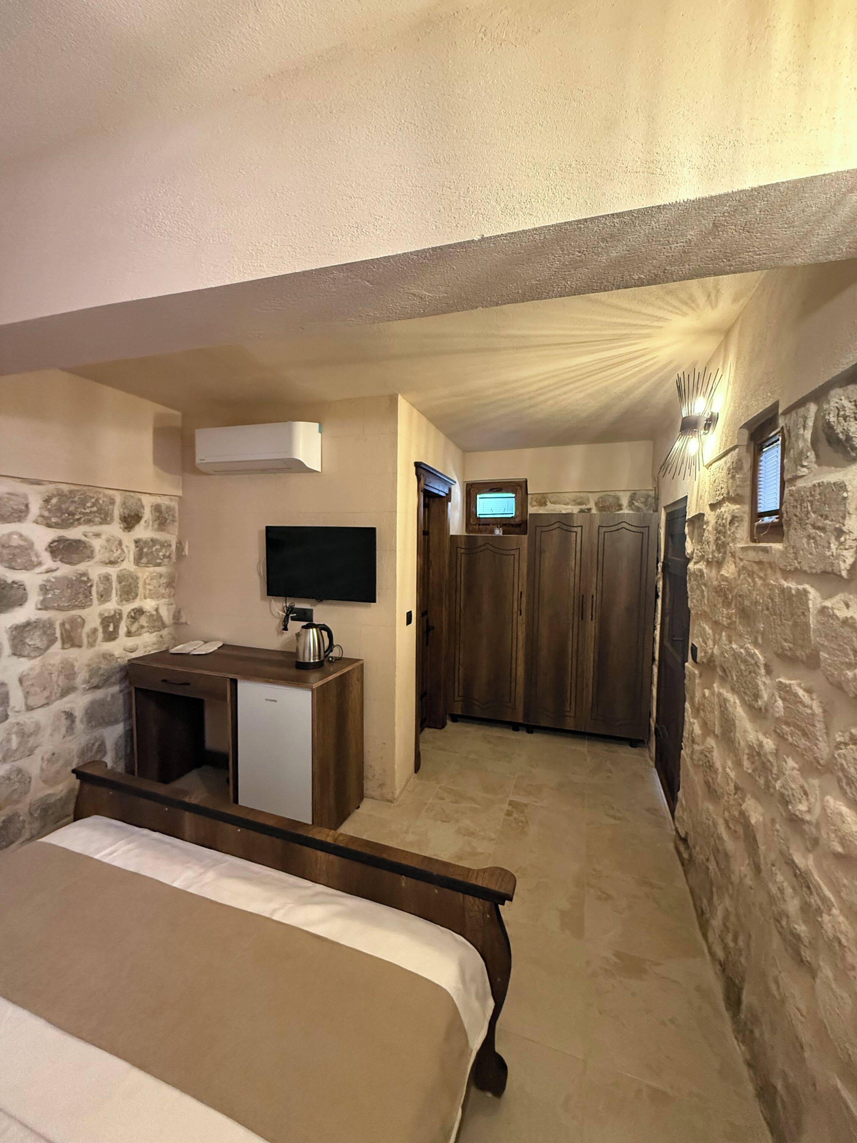 A bedroom with a bed, a small desk with a kettle, a TV, and a wardrobe.