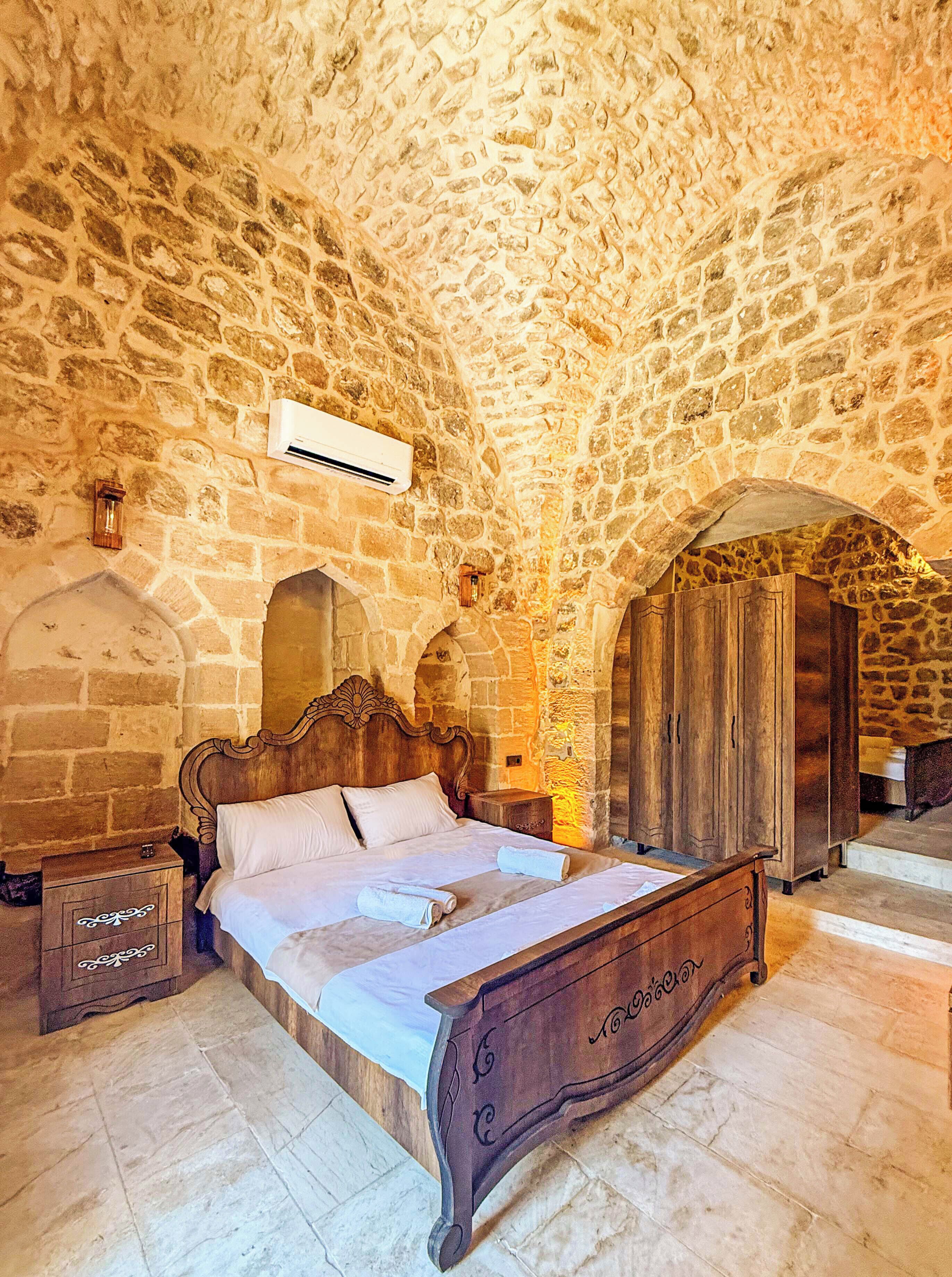 Un dormitorio con techo de piedra, cama de madera, mesita de noche y armario.