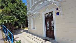 Um edifício com fachada branca, guarda-corpo de metal azul e porta castanha com detalhes em metal decorativo.
