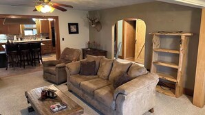 A living room with a sofa, coffee table, and a wooden bookshelf. - Experience a Farm getaway! (Bagley)
