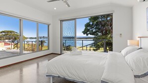 Et soveværelse med en stor seng, udsigt til søen og en balkon med gelænder.