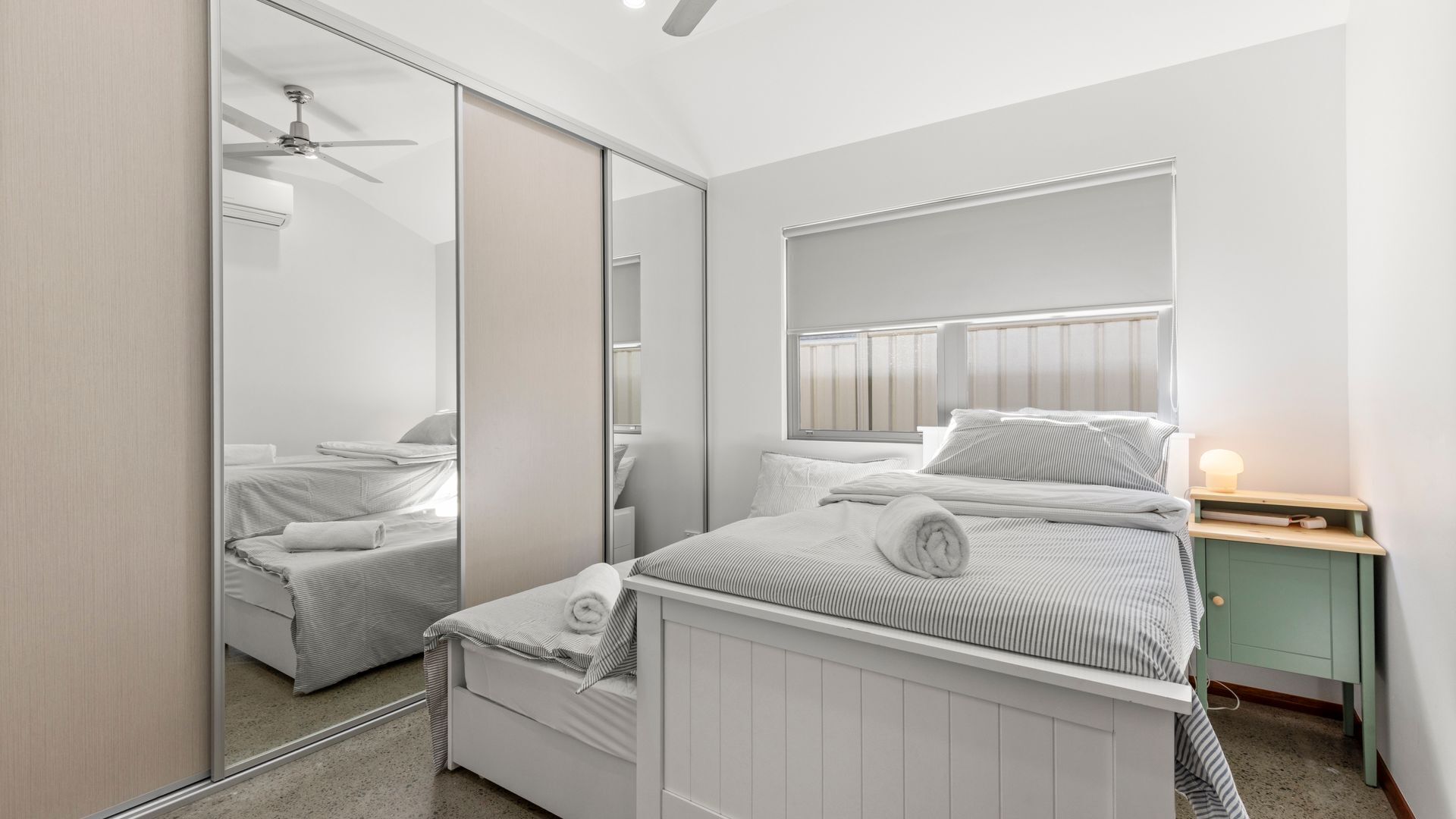 A bedroom with a bed, a bedside table, a mirror, and a ceiling fan.