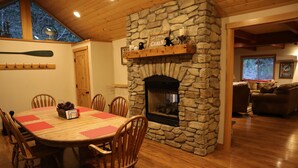 Una chimenea de piedra con un estante arriba, una mesa de comedor con sillas y vistas al exterior a través de una ventana.
