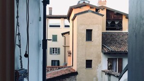 A balcony with a view of adjacent buildings, a metal railing, and a vent.
