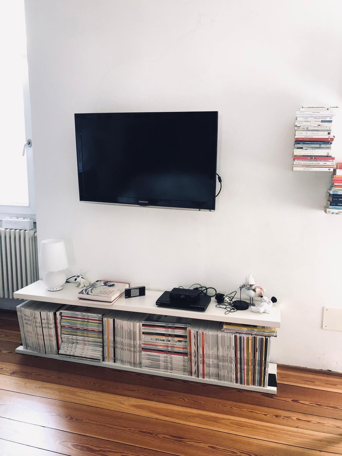 A modern living room with a flat-screen TV mounted on the wall, a white console table with books and a lamp, and a bookshelf filled with books.
