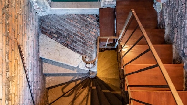 A spiral staircase with wooden steps and metal railings, leading to a lower level.