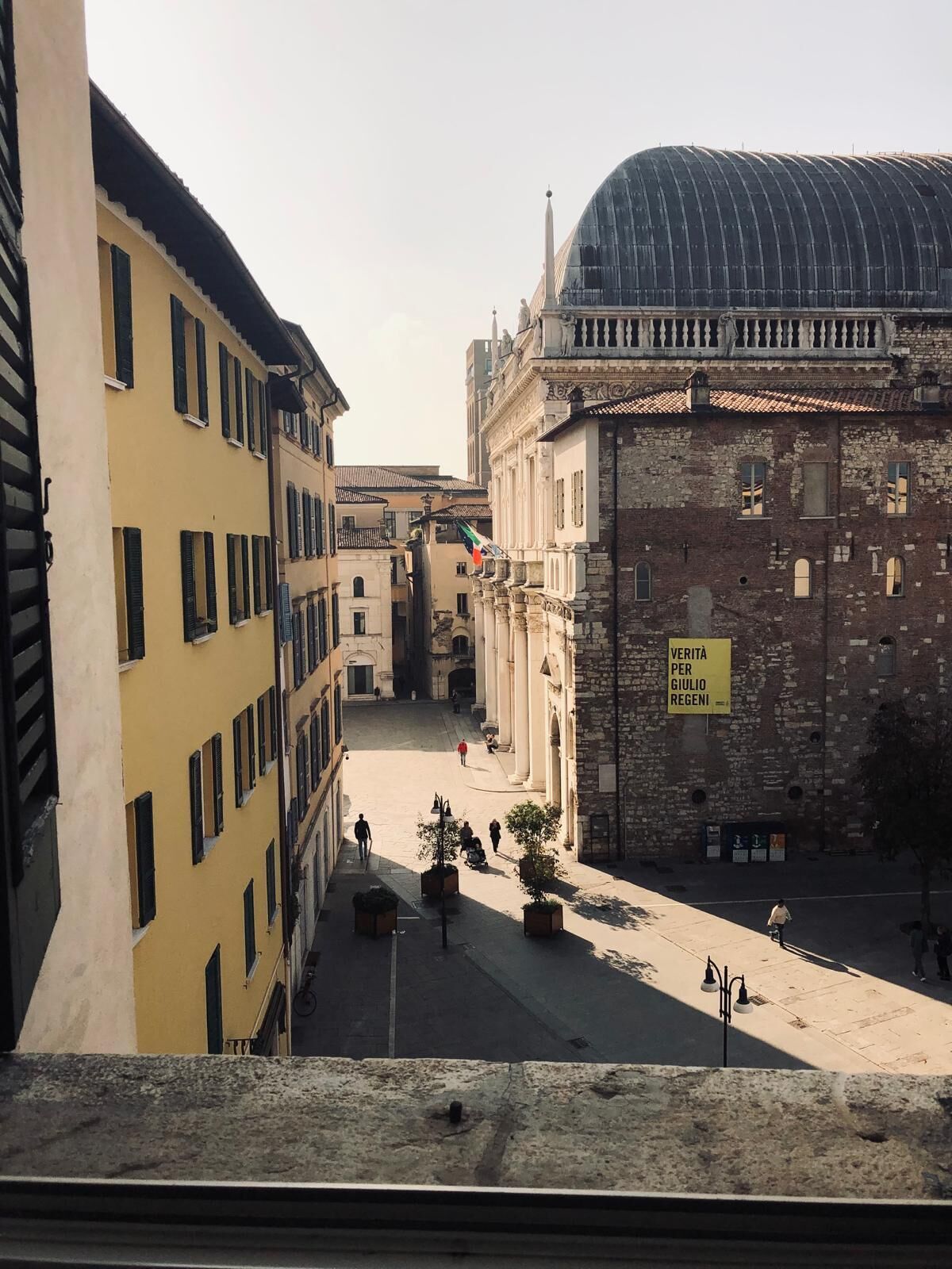 A historic building with a dome and columns, a courtyard with potted plants, and a sign in Italian.