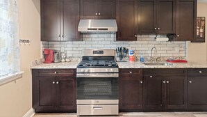 Una cocina con armarios de madera oscura, estufa de acero inoxidable, horno empotrado, campana de acero inoxidable, encimera de mármol y salpicadero azulejado.