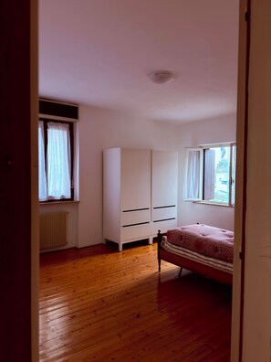 Ein Schlafzimmer mit Holzboden, einem Bett, einem Kleiderschrank und einem Fenster mit Vorhängen.