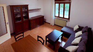 A room with a dining table, chairs, a sofa, a cabinet with glass doors, a window with curtains, and a radiator. - INDEPENDENT HOME FOR WORKERS AND FAMILIES in Orsaria (Orsaria)