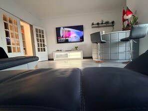 Un salon moderne avec un canapé en cuir, un téléviseur à écran plat, un comptoir de bar gris et un meuble blanc.