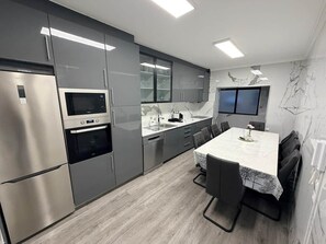 Une cuisine moderne dotée d’appareils électroménagers en acier inoxydable, un coin repas avec une table et des chaises, et un téléviseur à écran plat fixé au mur.