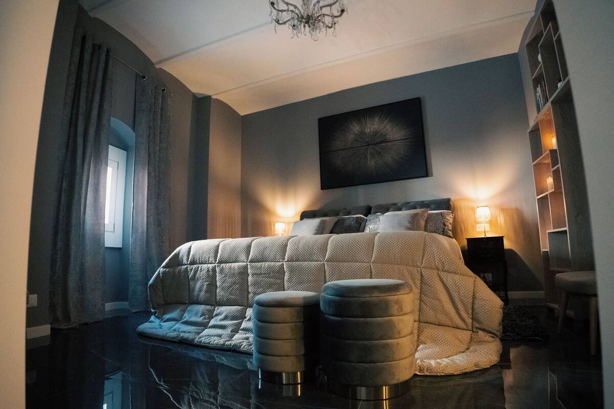 Une chambre à coucher avec un grand lit, deux tables de chevet, un lustre et un tableau au mur.