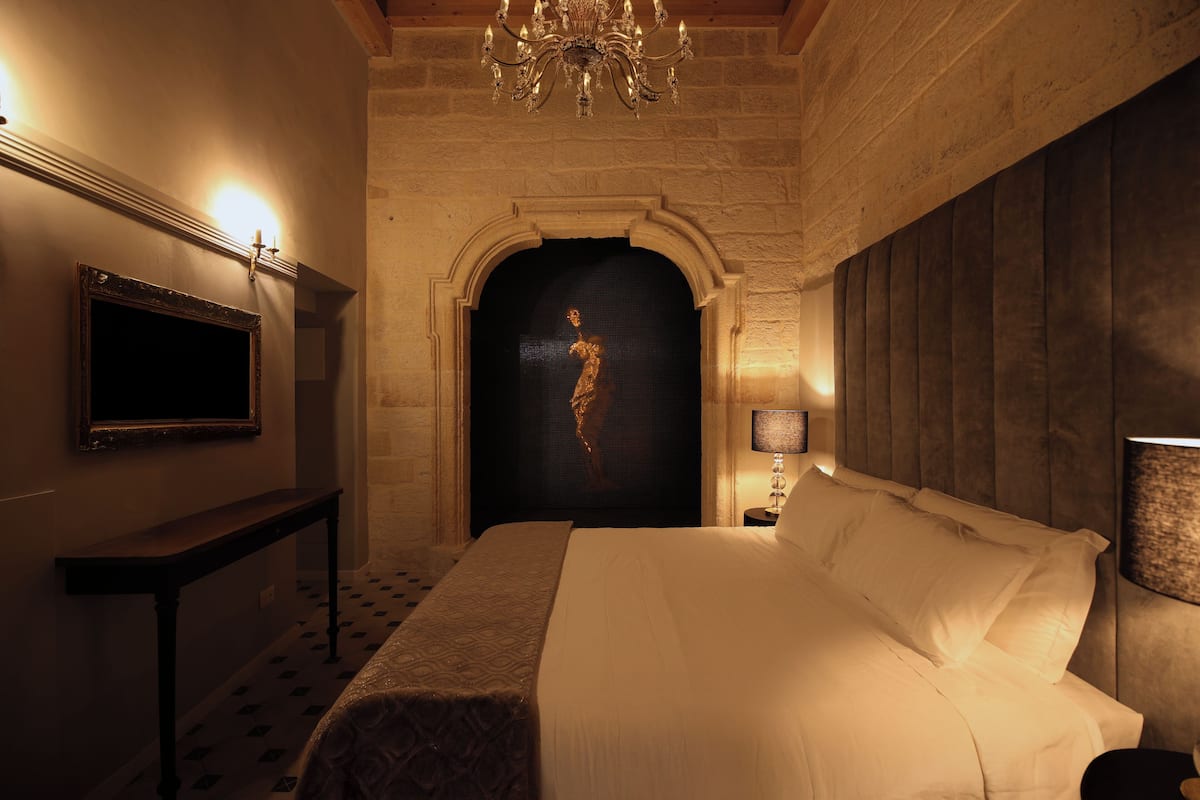 A hotel room with a bed, a television, a chandelier, and a statue.