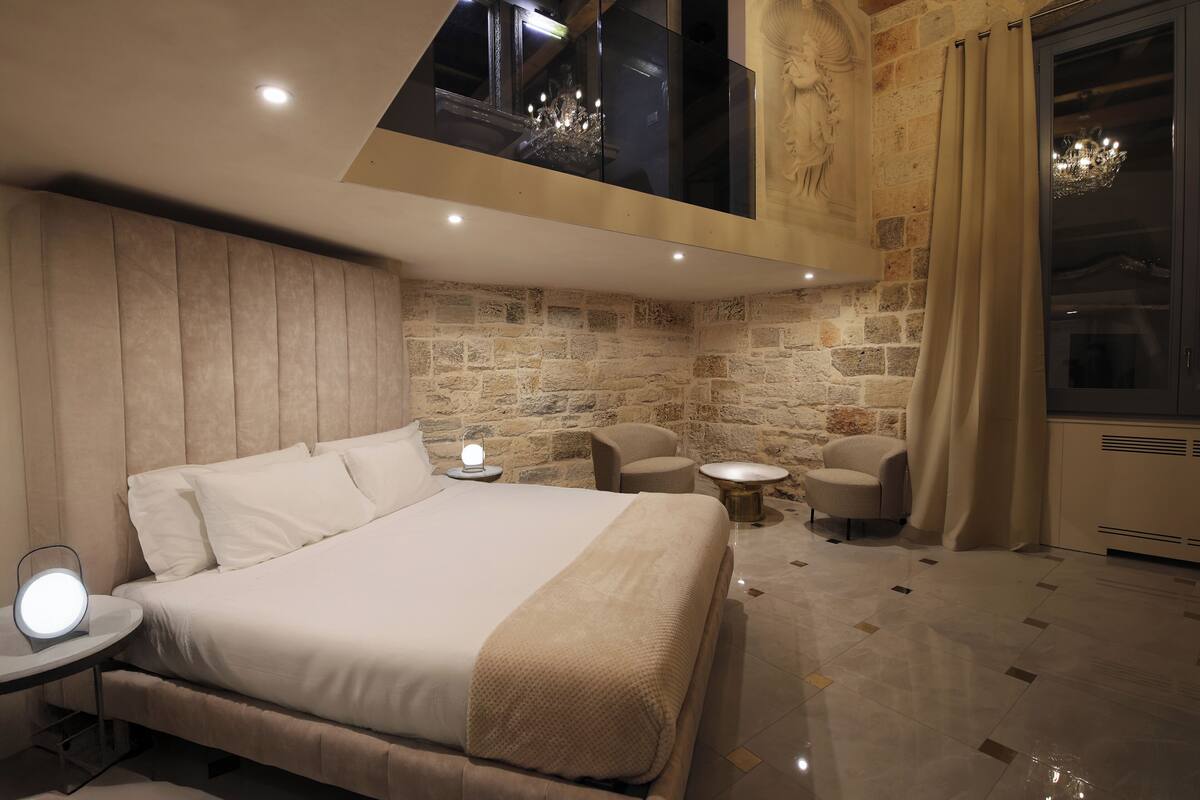Une chambre moderne avec un grand lit, une table de chevet avec une lampe, une petite table ronde et une chaise.