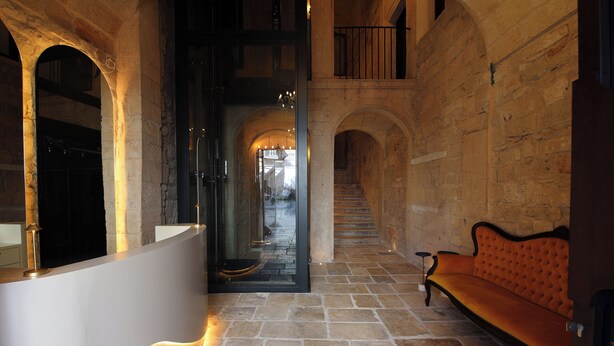 A stone-floored corridor with a reception desk, a bench, and an open doorway leading to a staircase. - The Duchess of Puglia (Polignano a Mare)