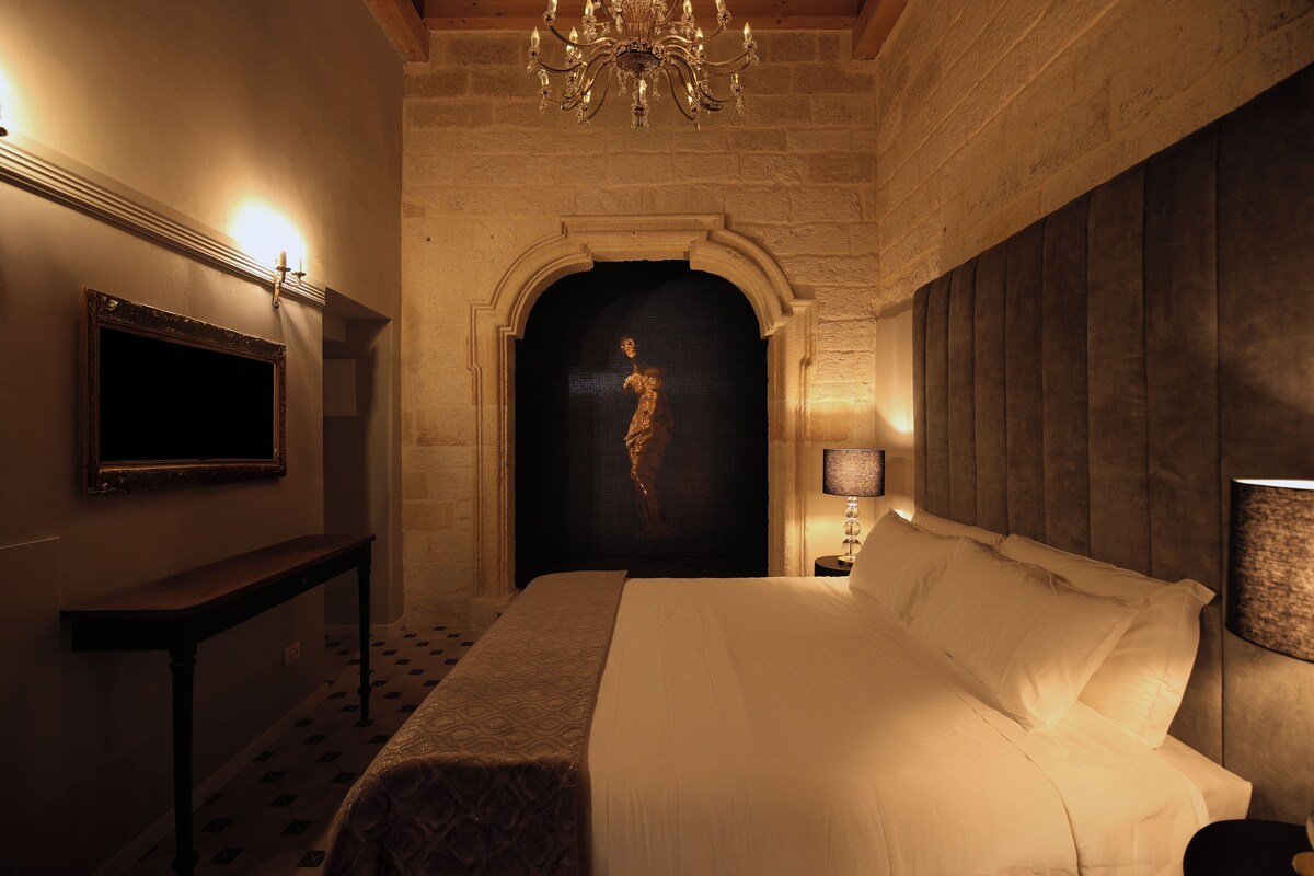 A hotel room with a bed, a television, a chandelier, and a statue.