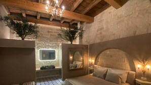A bedroom with a bed, a mirror, a chandelier, and a stone wall. - The Duchess of Puglia (Polignano a Mare)