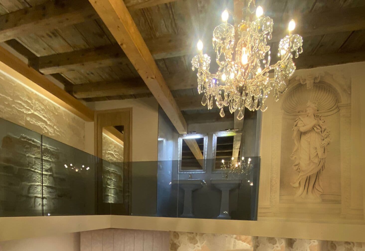 A room with a wooden ceiling, a chandelier, a glass railing, and a statue.