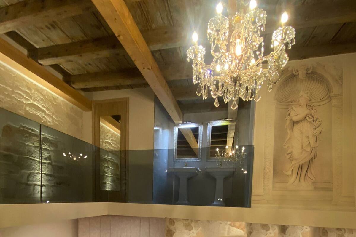 Une pièce avec un plafond en bois, un lustre, une balustrade en verre et une statue.