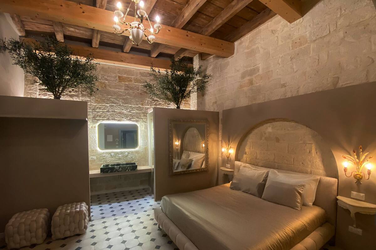 Une chambre à coucher avec un lit, un miroir, un lustre et un mur en pierre.