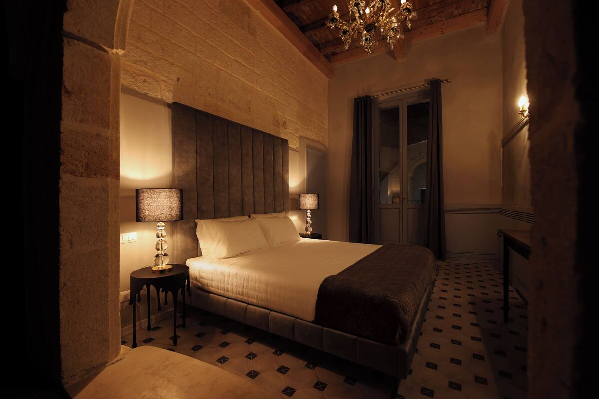 Une chambre à coucher avec un grand lit, deux lampes de chevet, un lustre et un sol à motifs.
