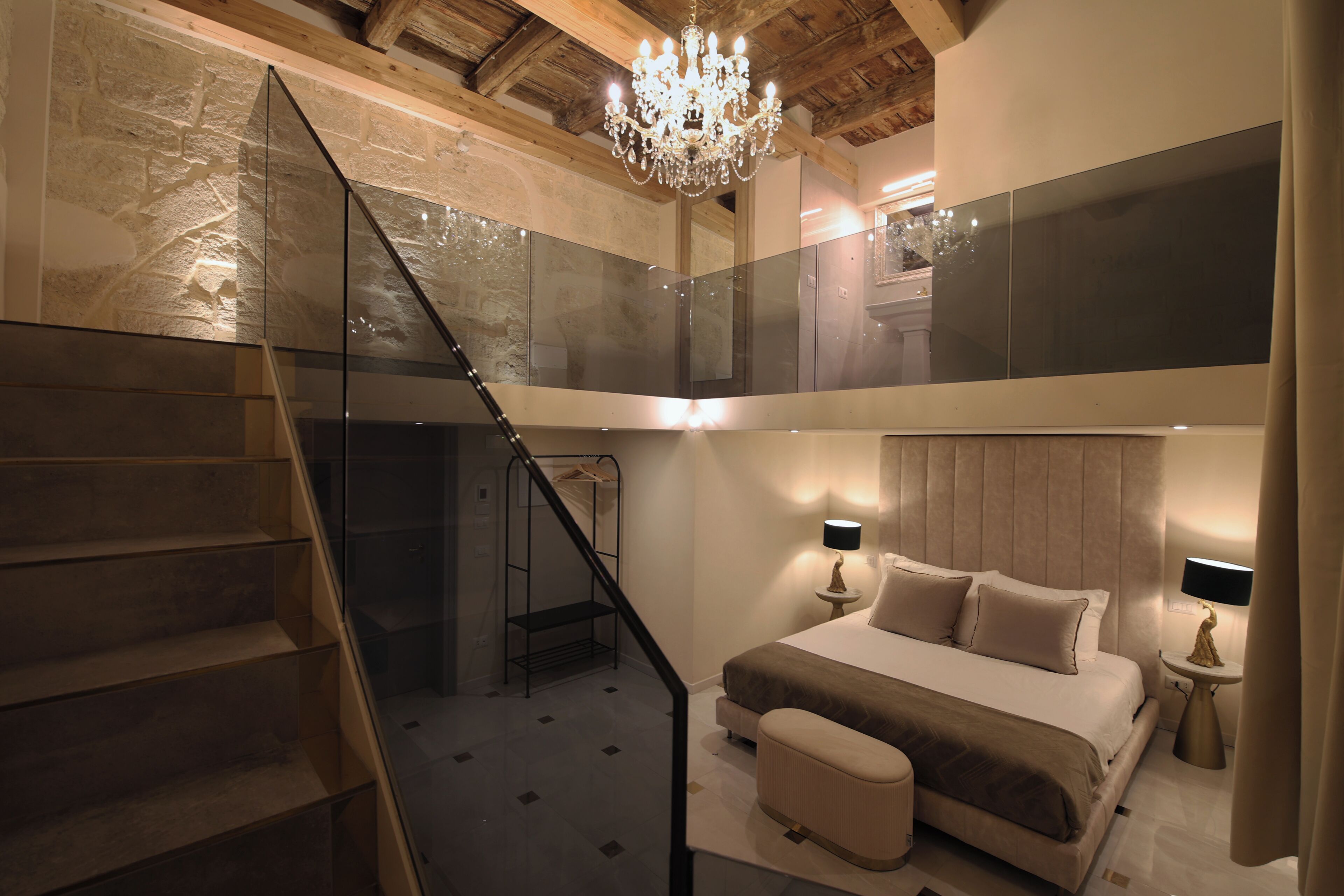 A bedroom with a bed, bedside table, lamp, and a staircase leading to an upper level.