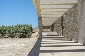 A stone corridor with steps leading to a door, surrounded by a stone wall and a clear sky. - Aetoula: Charming Stone Cave House with Sunset Views in Mylopotas (Ίος)