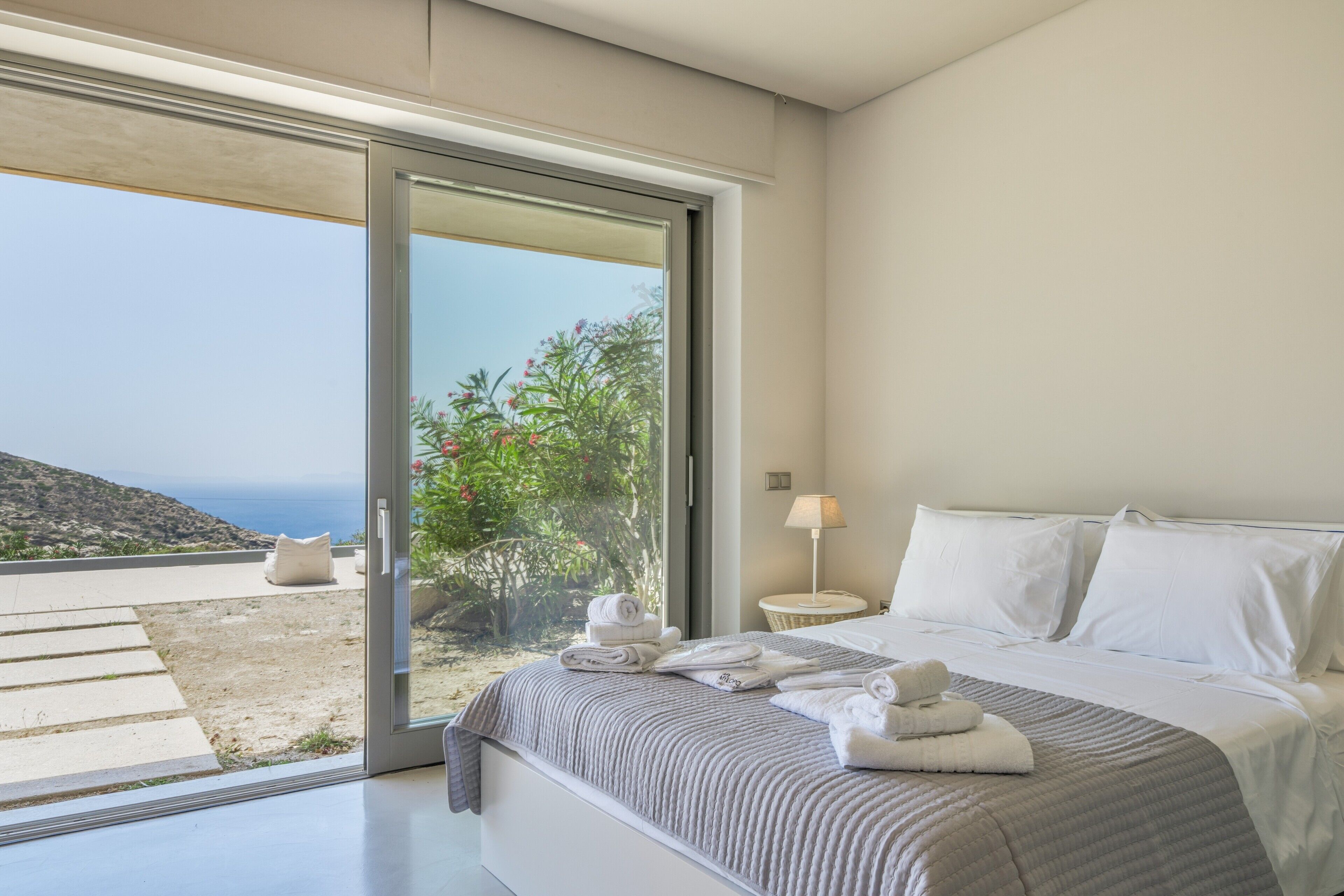 A bedroom with a bed, a nightstand, a lamp, and a view of the outdoors.