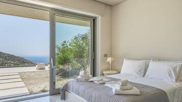 A bedroom with a bed, a nightstand, a lamp, and a view of the outdoors.