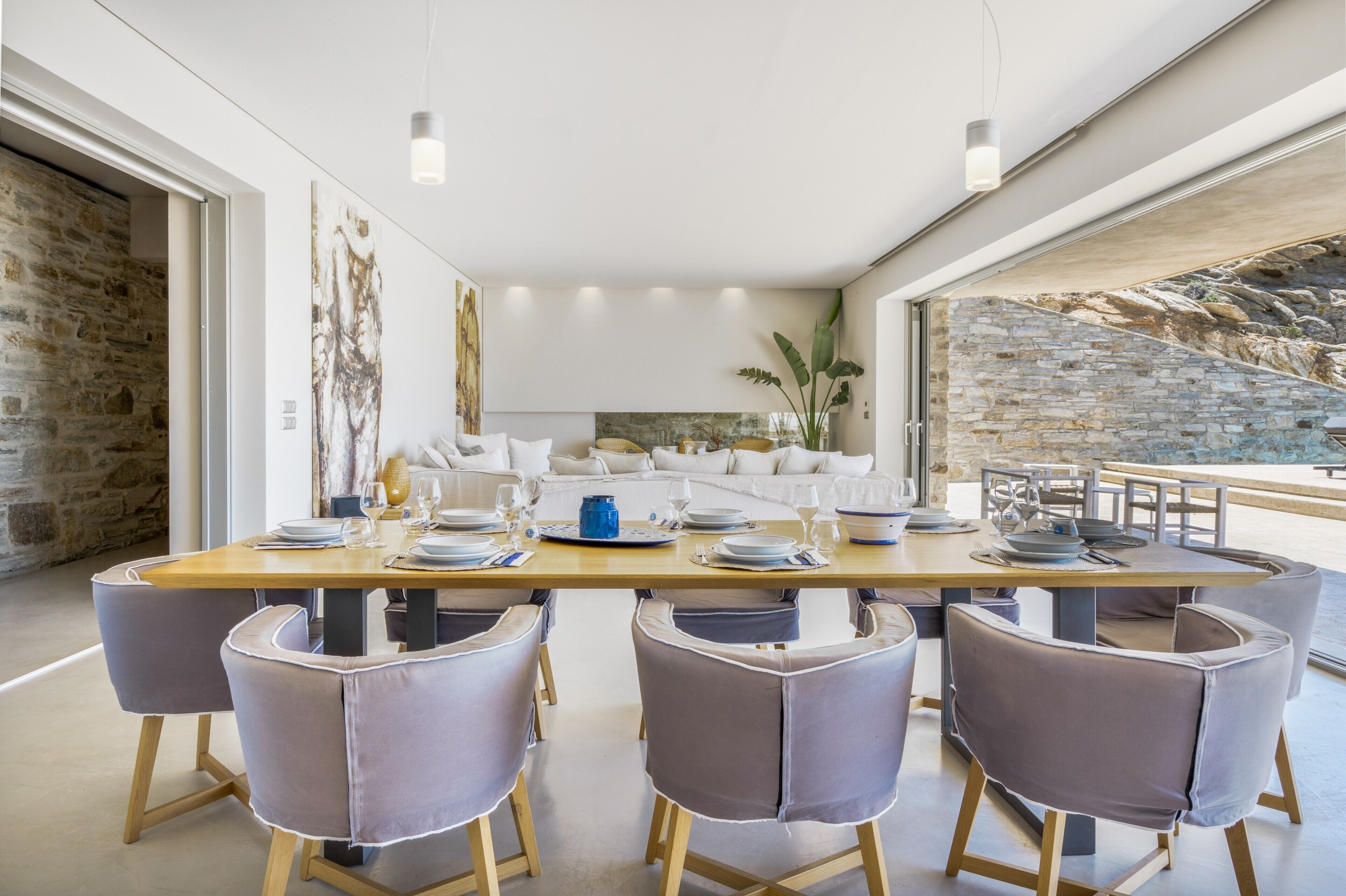 A modern dining area with a long table, six chairs, and a stone wall backdrop.