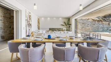 A modern dining area with a long table, six chairs, and a stone wall backdrop.