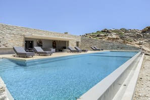 A swimming pool with lounge chairs, a stone building, and a rocky hillside.