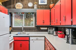 A compact kitchen with red cabinets, a Bosch dishwasher, a white refrigerator, and a window with a view of greenery.
