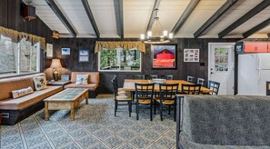 A cozy room with a wooden ceiling, a dining table with chairs, a sofa with cushions, and a patterned floor.