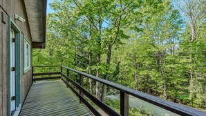A wooden deck with a railing overlooking a forested area with a river.
